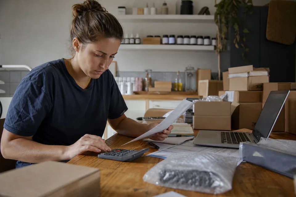 Online store owner checking a software subscription invoice with a calculator and laptop