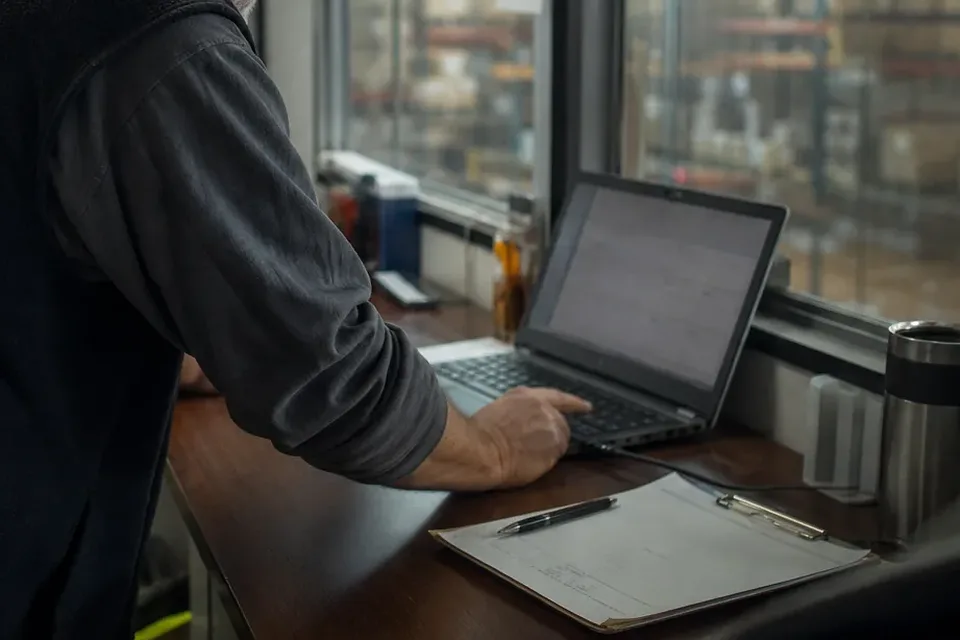 Account manager at a laptop with client notes on a clipboard
