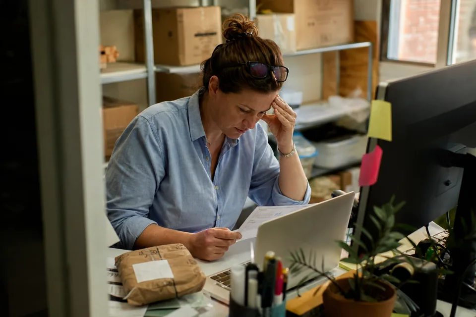 Support lead at a cluttered desk late in the day reading a customer question on a laptop